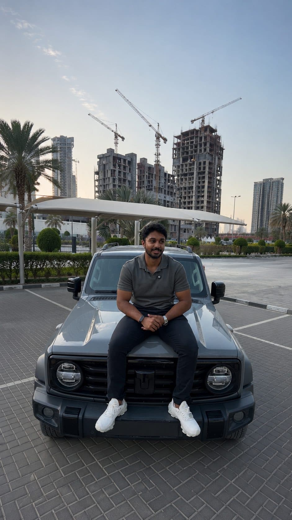 Suhayl seated on an SUV with the Dubai skyline at golden hour